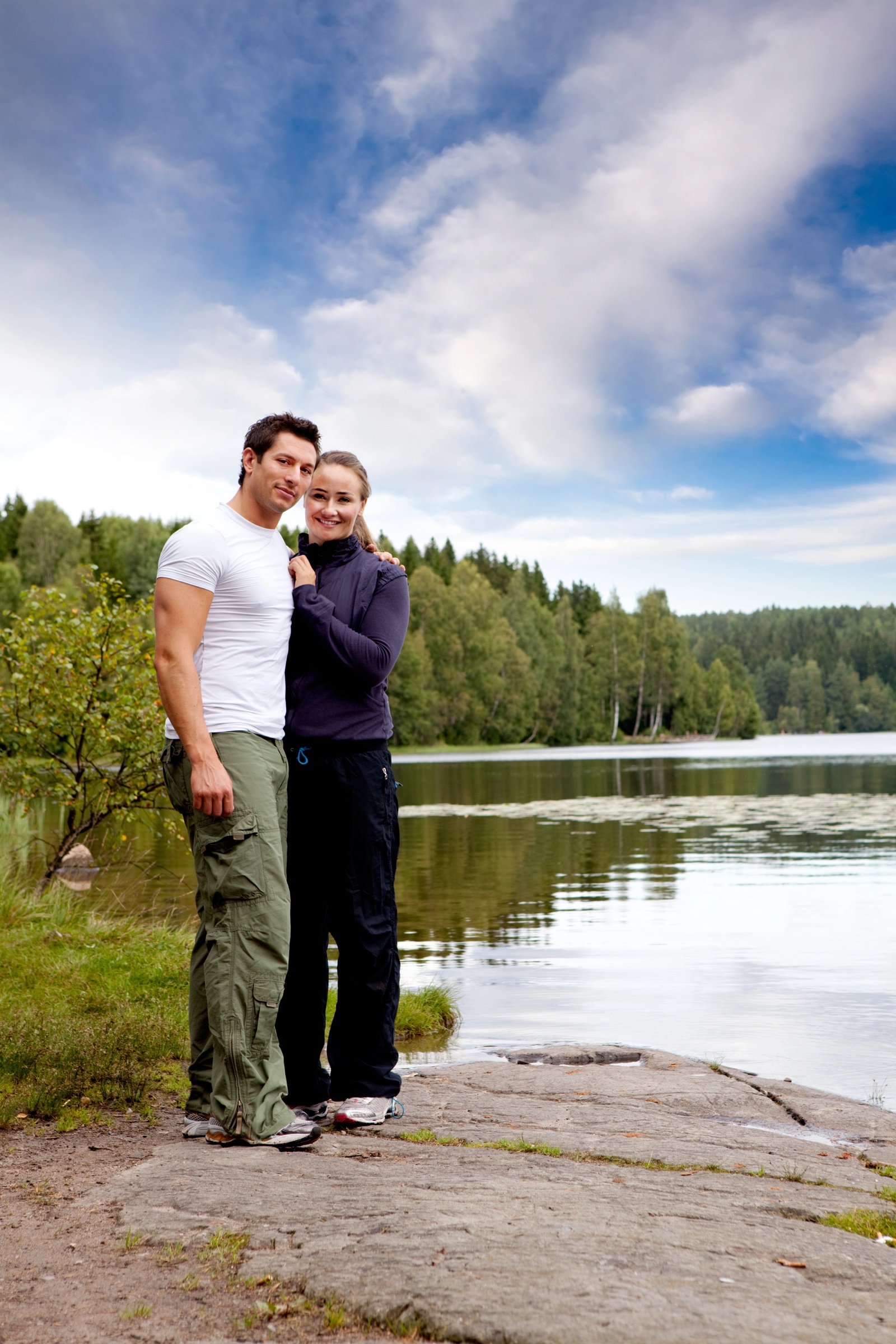 Source photo: a couple standing on a rock at the edge of a forest lake
